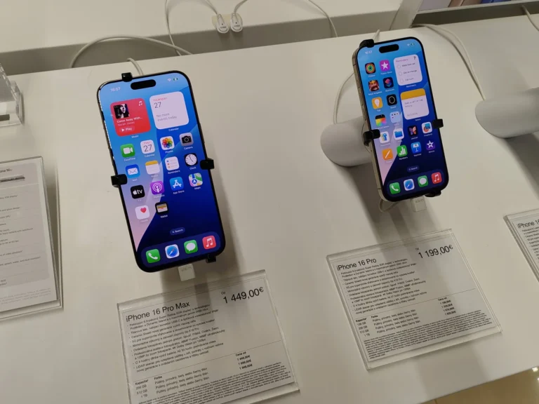 iPhone 16 Pro Max và iPhone 16 Pro đặt trên giá trưng bày của cửa hàng, màn hình đang bật