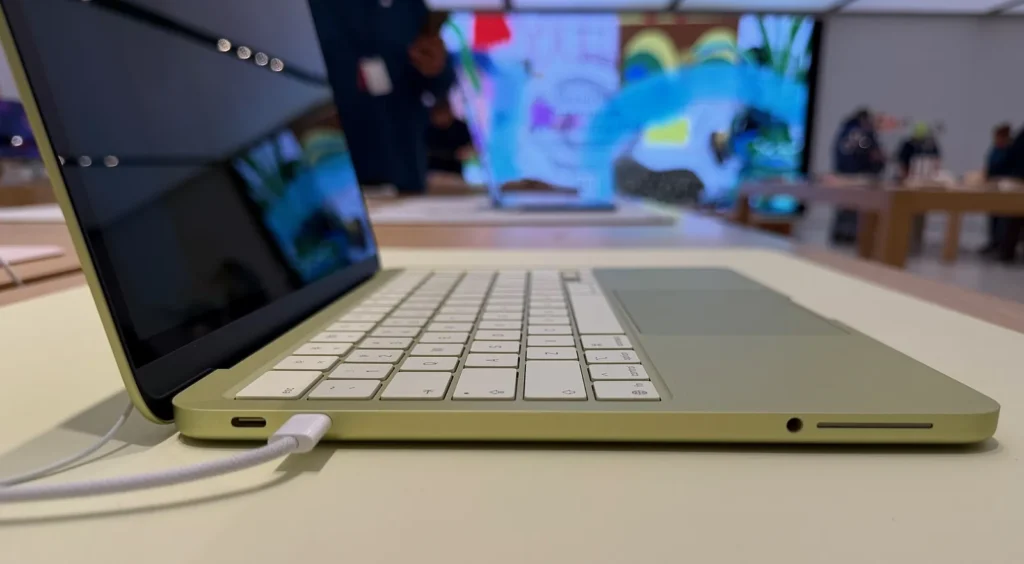 Cạnh trái MacBook Neo màu Citrus nhìn ngang: hai cổng USB-C, một cổng đang cắm cáp, và giắc tai nghe